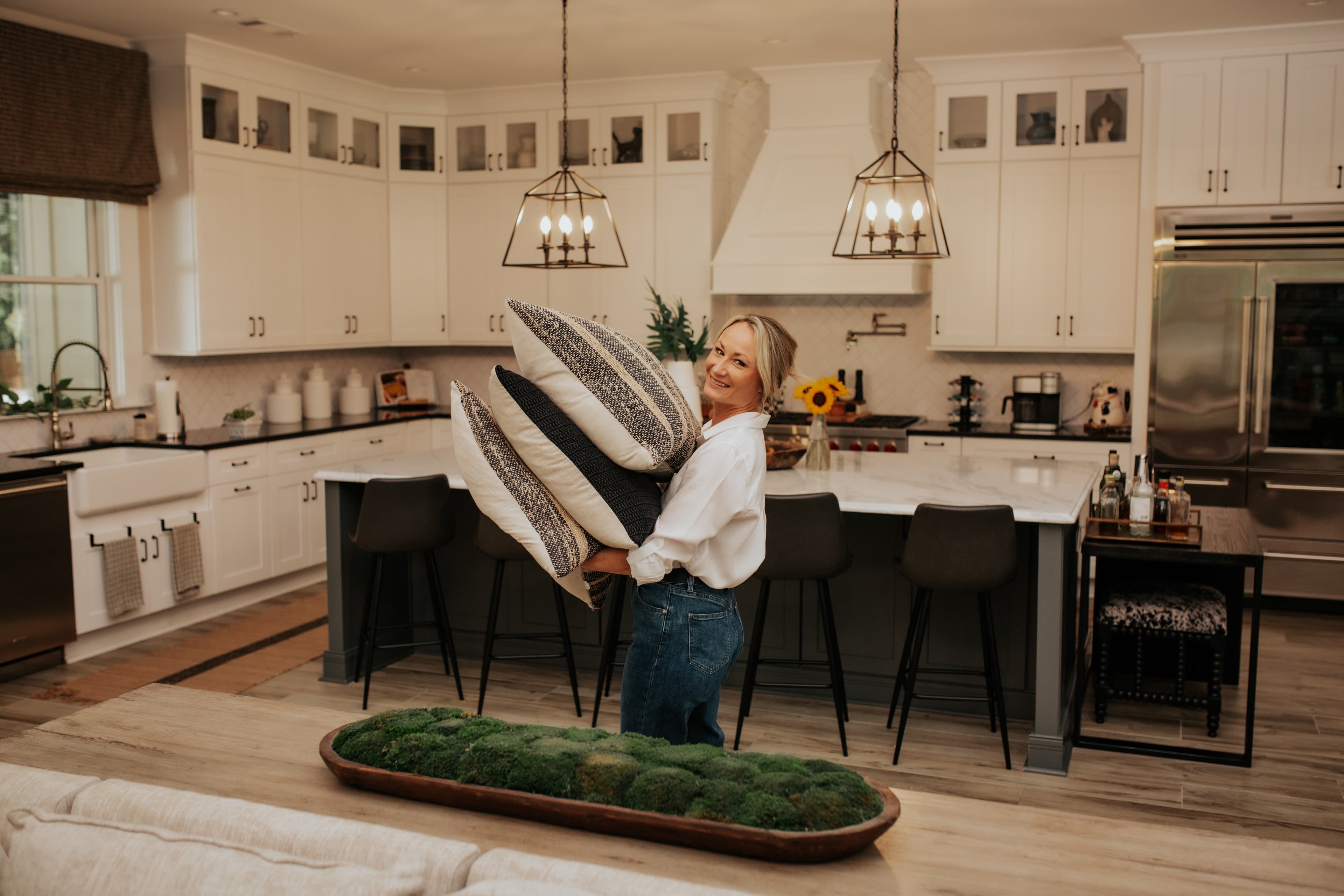 Lindsey Young carrying throw pillows through a client's kitchen, mid-styling session