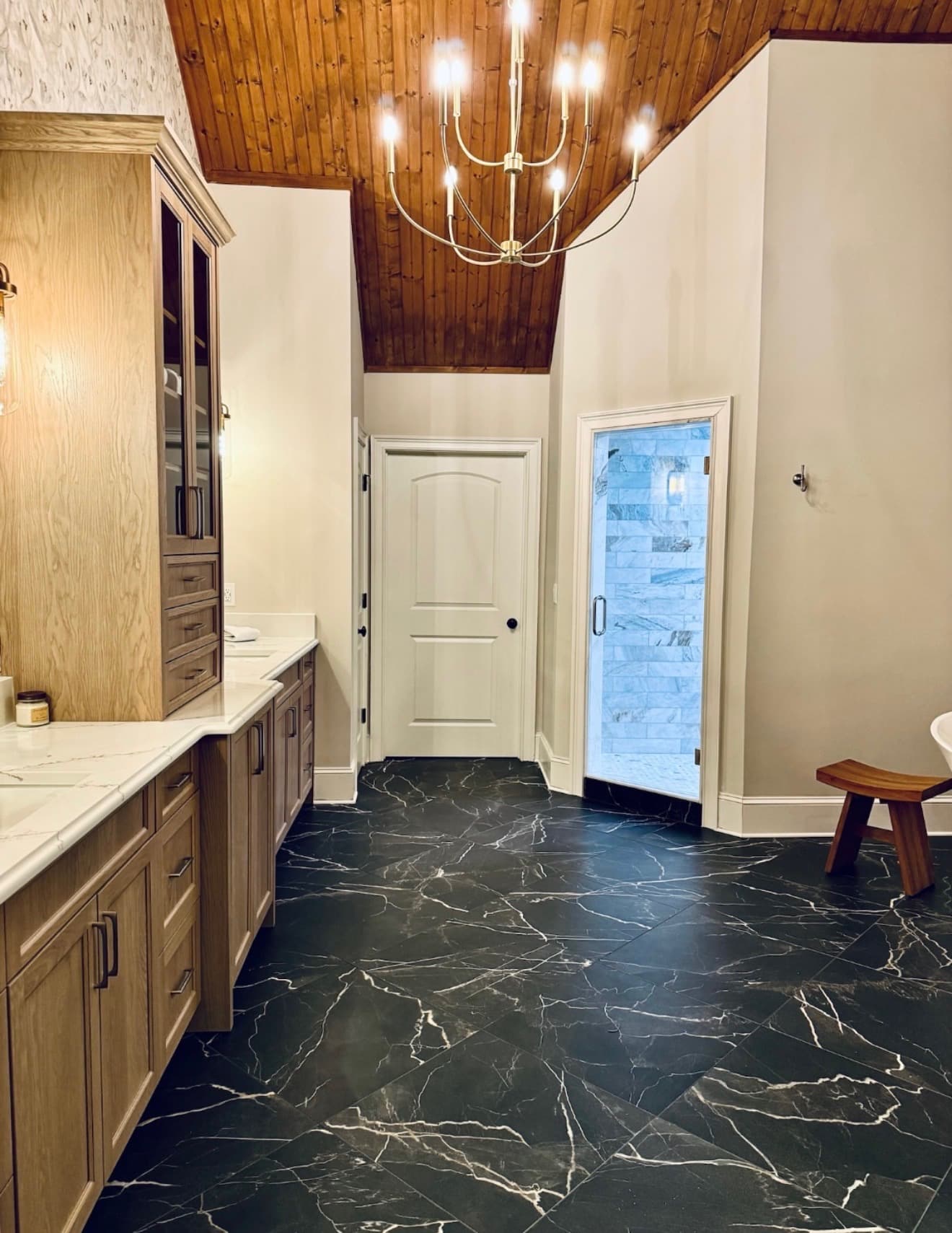 Primary bathroom with a vaulted wood ceiling, black marble floor, and glass shower