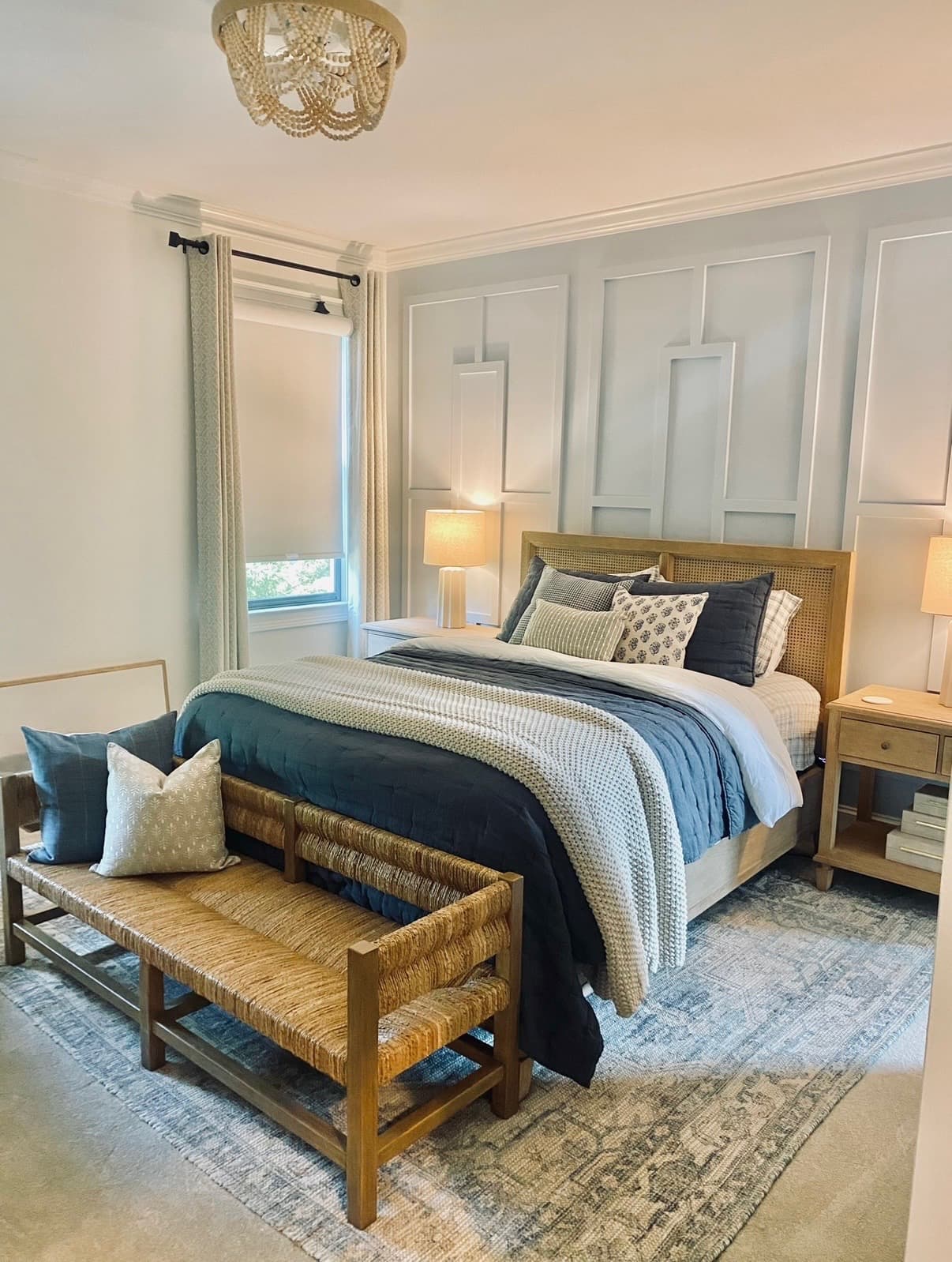 Primary bedroom with a rattan bench, layered pillows, and a cane bed frame against a paneled accent wall