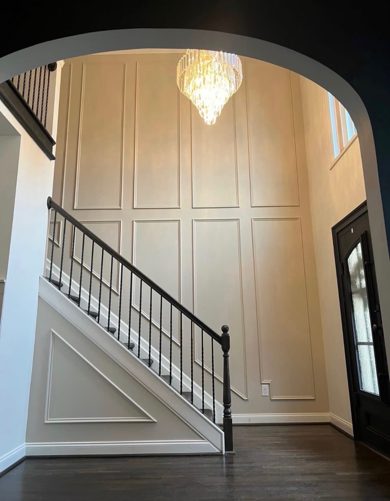 Two-story foyer with a curved archway, wainscoted accent wall, and a crystal chandelier over the staircase
