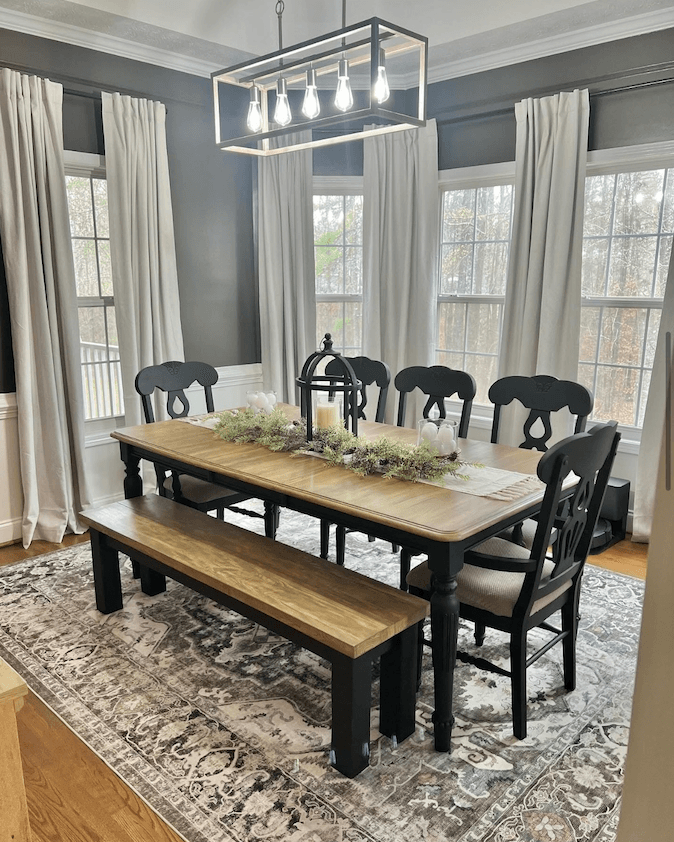 Staged dining room with a black wood table, bench, upholstered chairs, and a patterned area rug