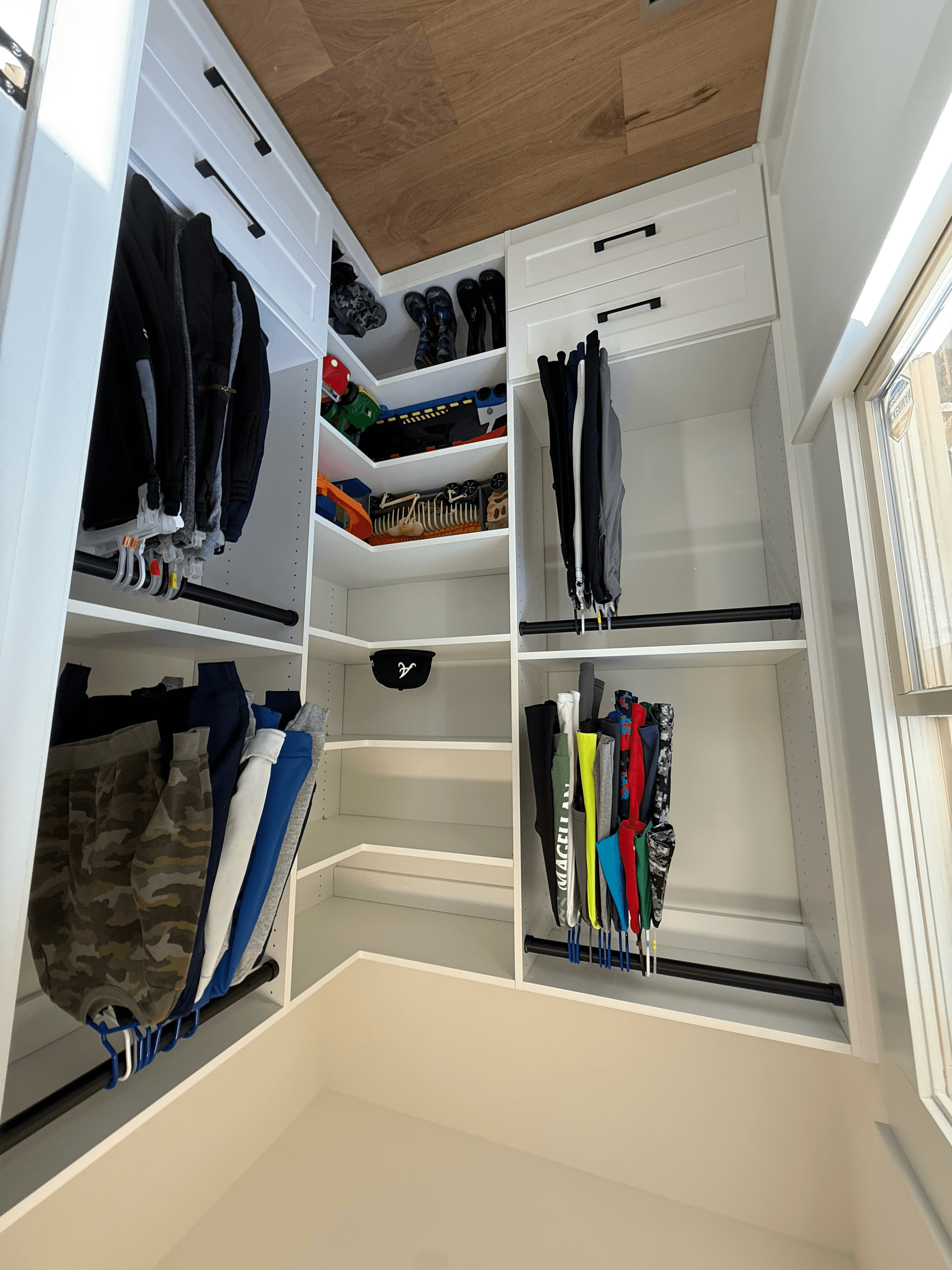 Corner of an organized kids' closet with labeled clothing rods, shoe cubbies, and toy storage