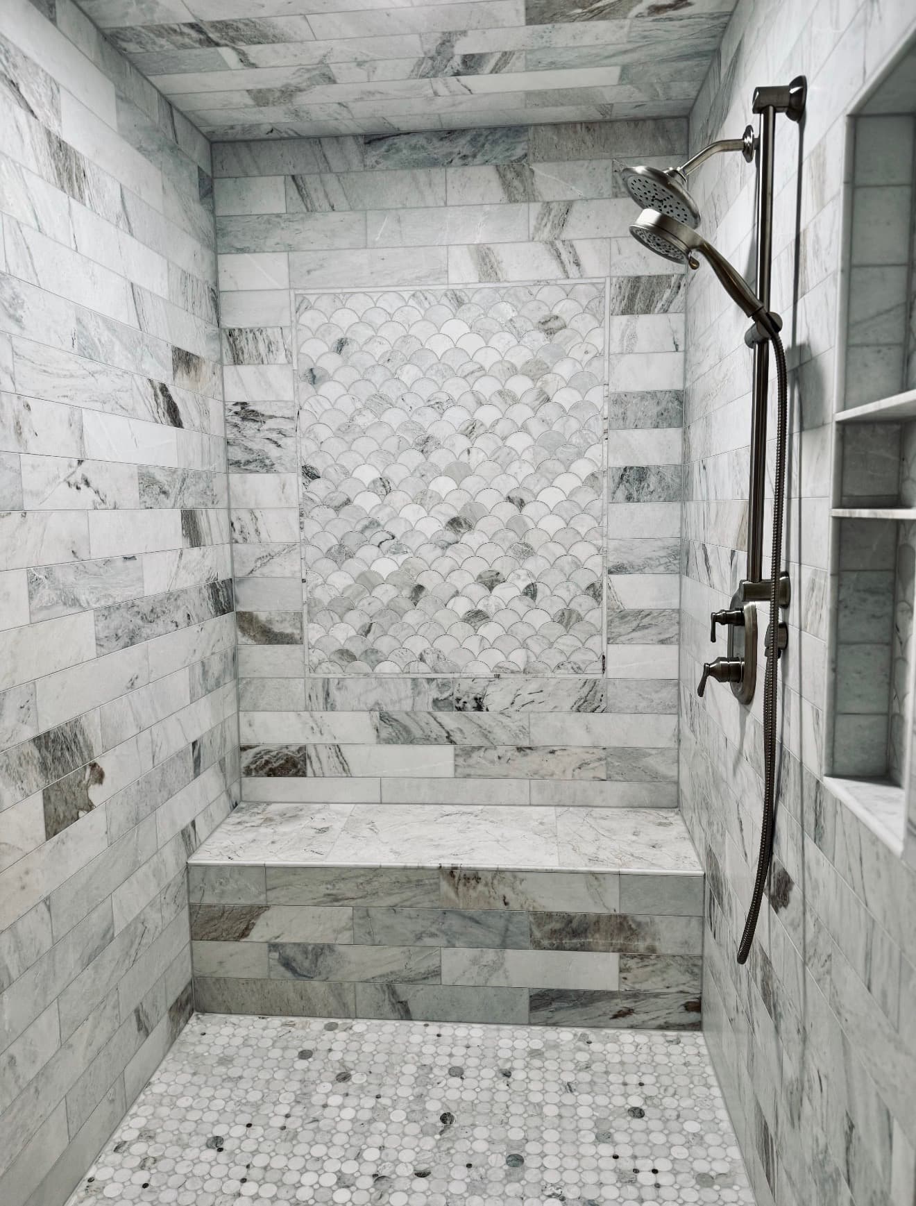 Fish-scale mosaic tile accent inside a marble-tiled walk-in shower with a built-in bench